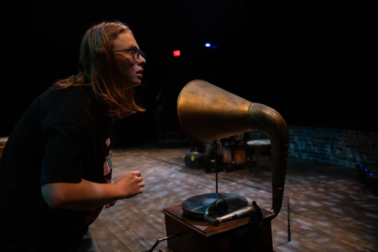 A performer leans toward an antique gramophone on the stage.