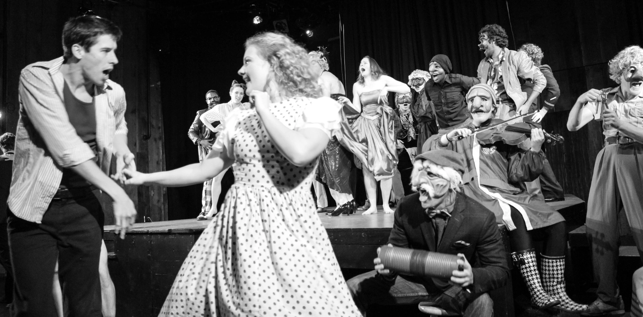Black-and-white photograph of the Viva Commedia ensemble performing with masks and musical instruments.